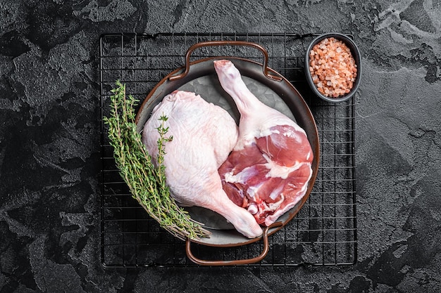 Raw Free range duck legs in a steel tray with thyme Black background Top view