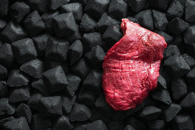 Raw fresh beef meat over a charcoal with copy space top view 