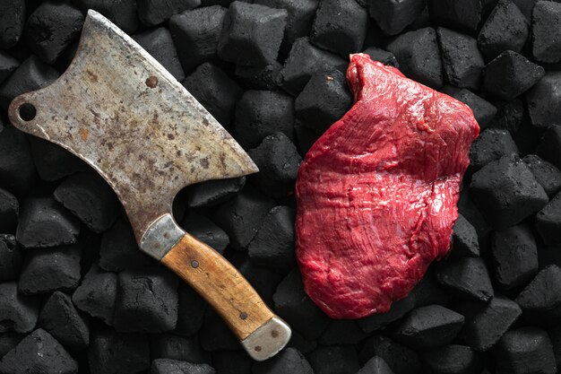 Raw fresh beef meat with old butcher knife over a charcoal top view