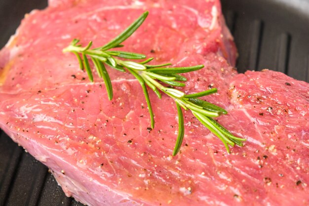 Raw fresh beef steak with a rosemary on a grill pan.