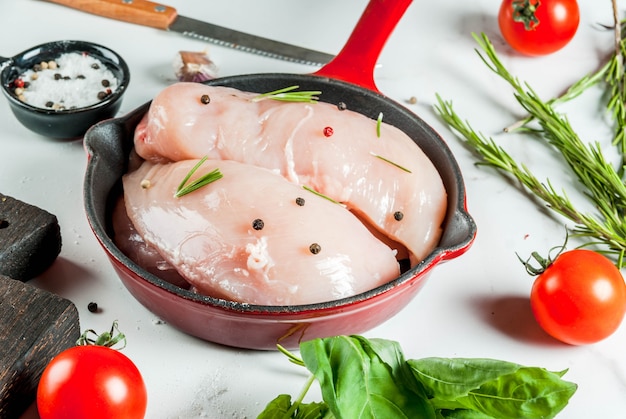 鉄の鋳鉄フライパンで調理するためのハーブとスパイスを入れた生の新鮮な鶏の胸肉の切り身、白い大理石のテーブル