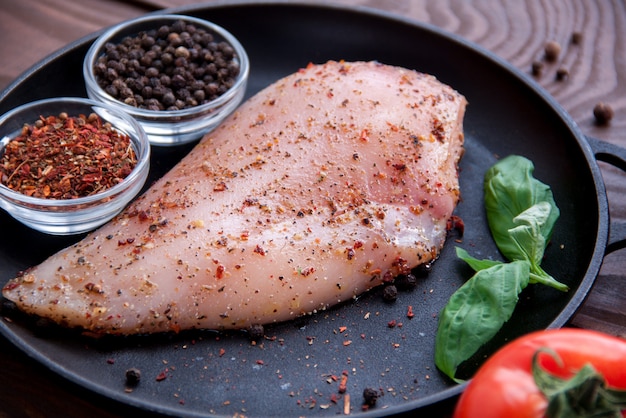 Il filetto di pollo fresco crudo con spezie ed erbe aromatiche si trova su una padella di ferro nero