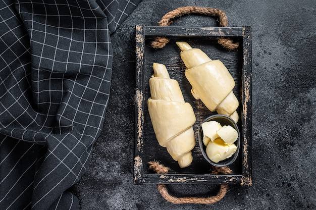 Raw fresh croissant in a wooden tray. Black table. Top view.