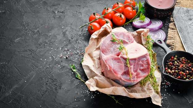 Photo raw fresh cross cut veal shank for making osso buco with spices and herbs on a black background top view free space for your text
