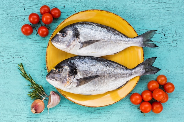 Сырая свежая рыба дорадо на тарелке и овощах на синем фоне. Вид сверху.
