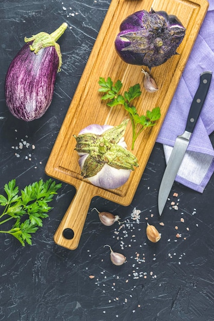 Raw fresh eggplant on wooden cutting board Concept of green house life style and products of subsistence farming flat lay on black concrete surface copy space