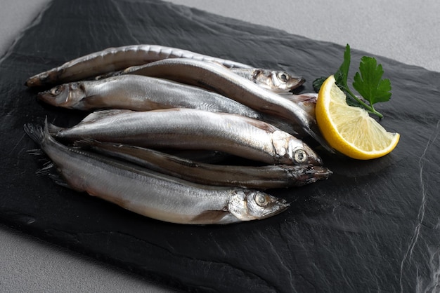 Raw fresh fish capelin with lemon gray background top view