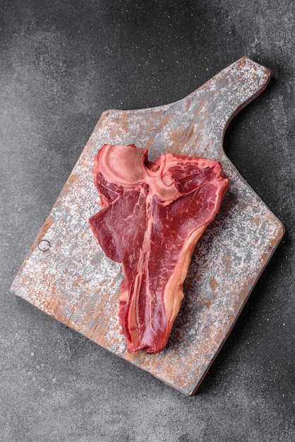 Raw fresh juicy beef tbone steak with salt spices and herbs on a dark concrete background