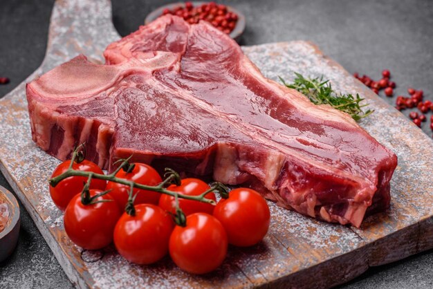 Raw fresh juicy beef tbone steak with salt spices and herbs on a dark concrete background