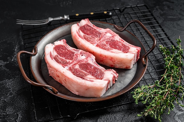 Raw fresh lamb loin chops with herbs and spices in steel tray Black background Top view