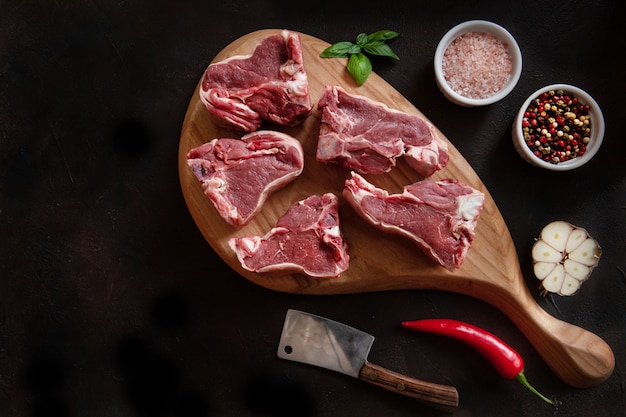 Costole e condimenti freschi crudi della carne di agnello sul tagliere di legno.