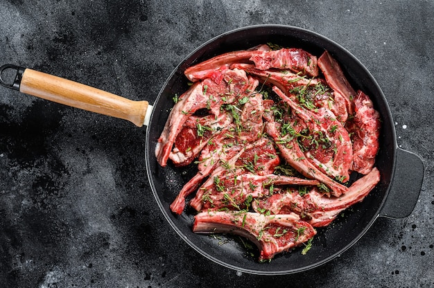 Raw fresh lamb rib chops marinated with thyme and mint in a pan. Black background