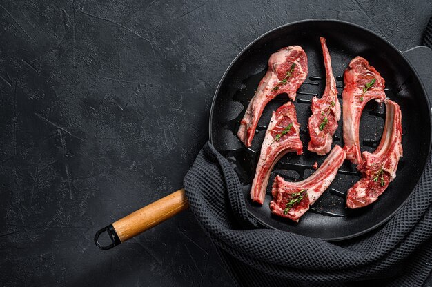 Raw fresh lamb rib chops with salt pepper and herbs in a pan