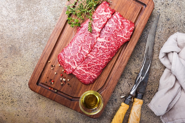 Crudo fresco di carne marmorizzata bistecca di manzo e condimenti sul tagliere sulla superficie della pietra, vista dall'alto