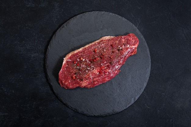 Raw fresh marbled meat and seasonings on dark ckground top vie