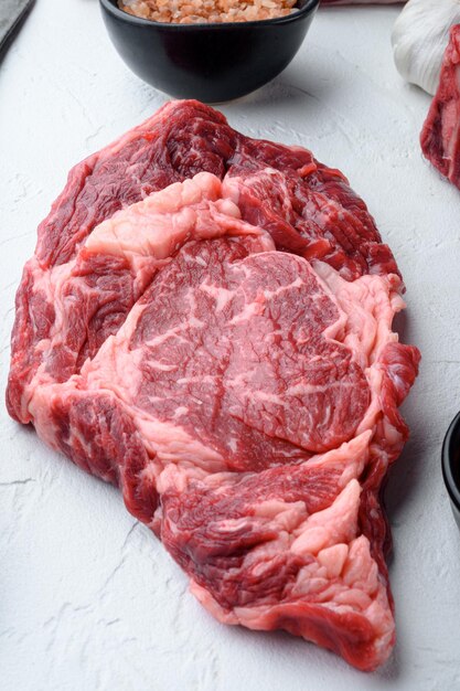 Photo raw fresh marbled meat steak ribeye black angus set, on white stone  background, top view flat lay