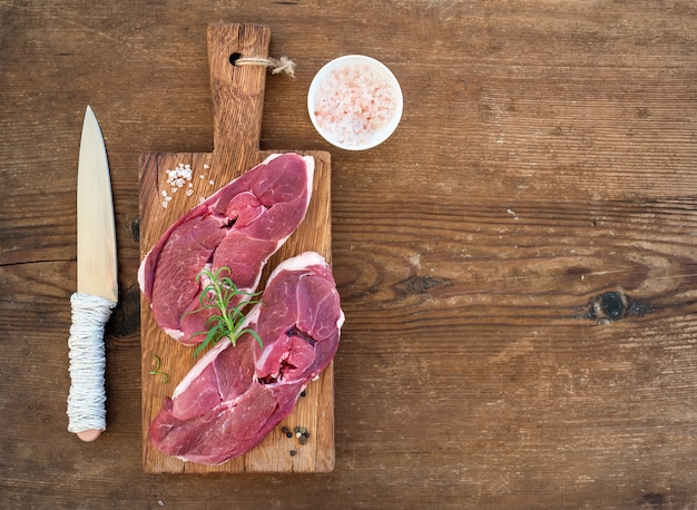 Raw fresh meat lamb entrecote and seasonings on cutting board over rustic wooden background.