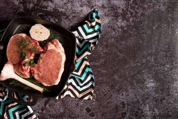 Bistecca di carne fresca cruda sulla griglia padella di ferro, condimento e forchetta di carne su legno