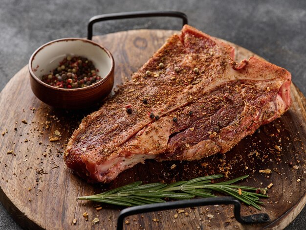 Raw fresh meat Tbone steak seasoning on chopping cutting wooden board on grey background