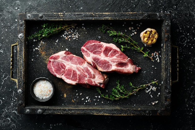 Raw fresh pork steaks with spices and herbs Top view On a black stone background