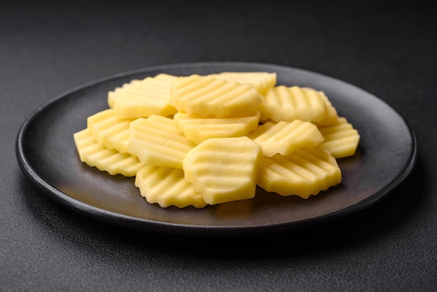 Raw fresh potatoes cut into slices on a black ceramic plate