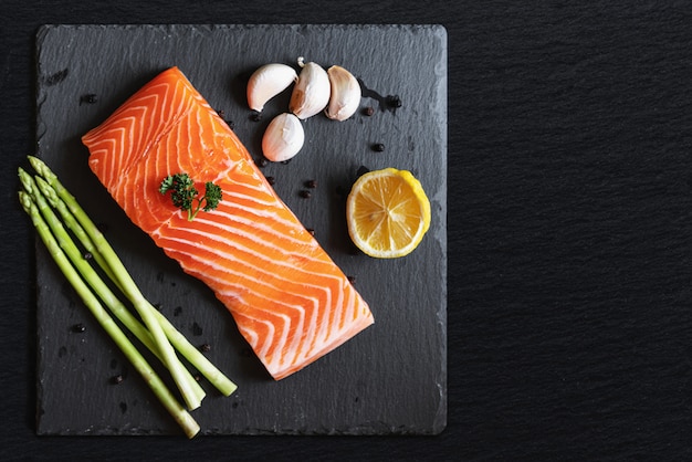 Raw fresh salmon fillet with herbs and ingredients, on black stone plate 