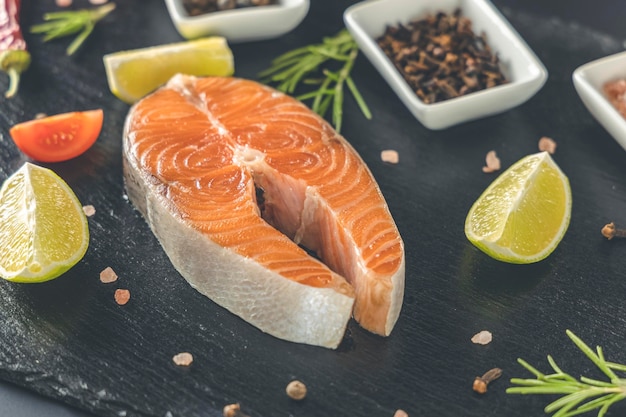 Photo raw fresh salmon steak on a slate board and salt peppers lemon cloves and rosemary around raw salmon red fish cooking salmon seafood healthy food concept salmon and spices
