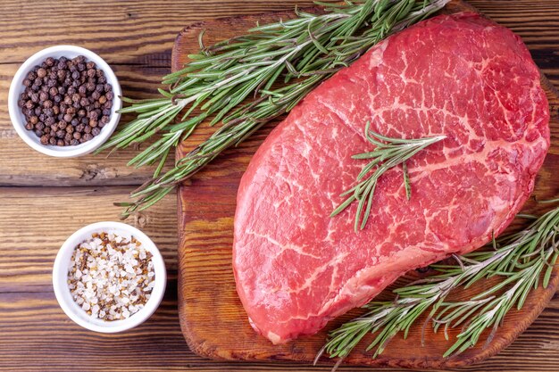 Raw Fresh Steak Served with Twigs of Rosemary and Herbs on Rustic Wooden Board