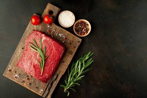 Raw fresh steak with herbs, on a cutting board, stone background, top view   with copy space for your text