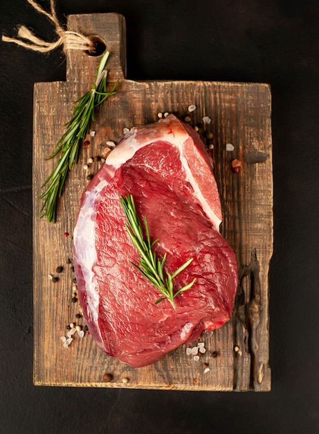 Raw fresh steak with herbs, on a cutting board, stone background, top view