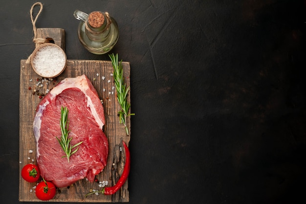 Raw fresh steak with herbs, on a cutting board, stone background, top view