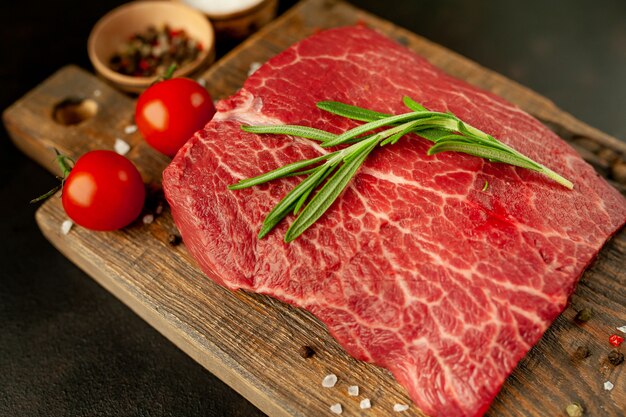 Raw fresh steak with herbs, on a cutting board, stone background, top view