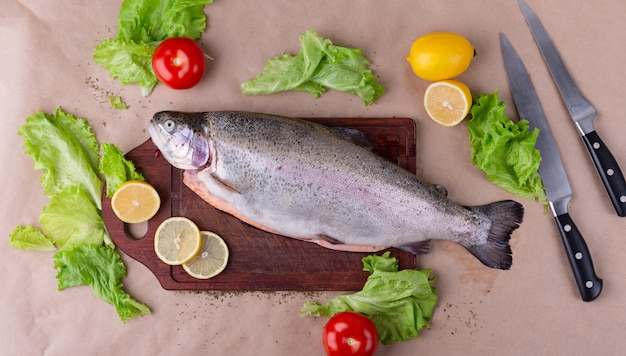 Raw fresh unprepared salmon fish on a wooden board with ingredients for cooking. Lemon, lettuce, tomatoes. Mediterranean cuisine