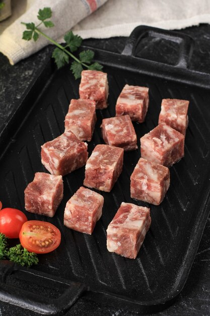 Cubetti di wagyu di saikoro congelati crudi o bistecca di manzo a dadi su piatto di bistecca nero con spezie e verdure