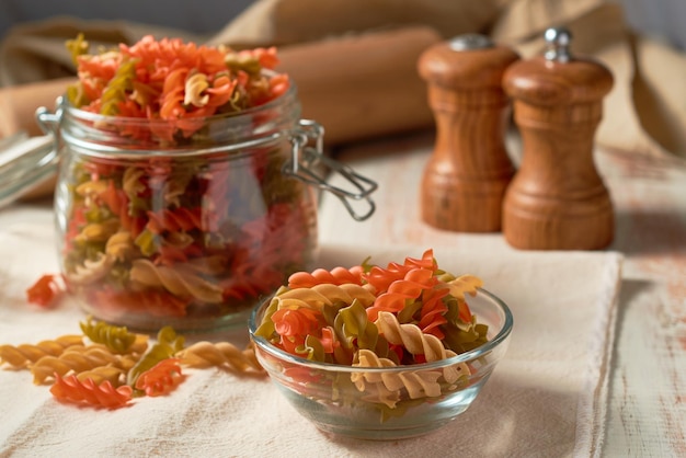 Raw fusilli pasta of different colors on a rustic background