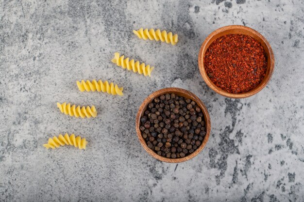 Raw fusilli pasta with various pepper spices on stone. 