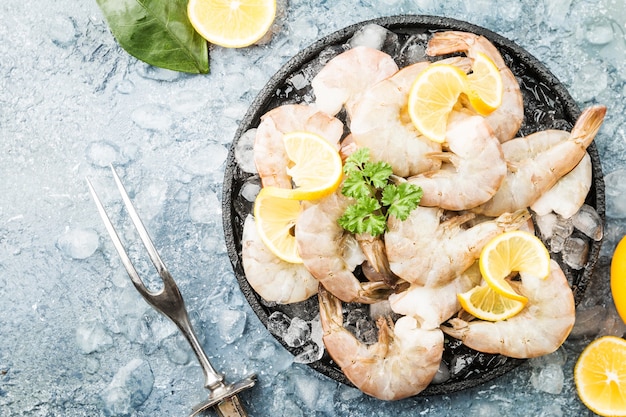 Raw giant shrimps with lemon and spices in a frying pan over gray