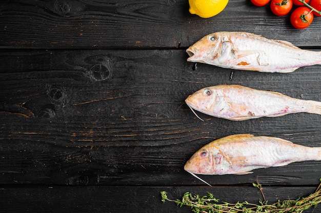 生のヒメジ新鮮な丸ごとの魚と黒の木製テーブルの背景に食材とハーブを含む上面図フラットはテキストのコピースペースで横たわっていた