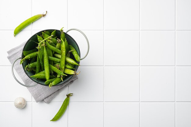 Raw Green Organic Snow Peas on white ceramic squared tile table background top view flat lay with copy space for text