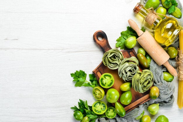 白い木製の背景にトマトオイルとパセリと生の緑のパスタイタリアの伝統的な料理新鮮な野菜トップビューあなたのテキストのための自由なスペース