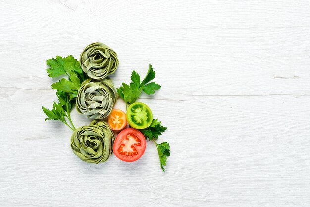白い木製の背景にトマトオイルとパセリと生の緑のパスタイタリアの伝統的な料理新鮮な野菜トップビューあなたのテキストのための自由なスペース