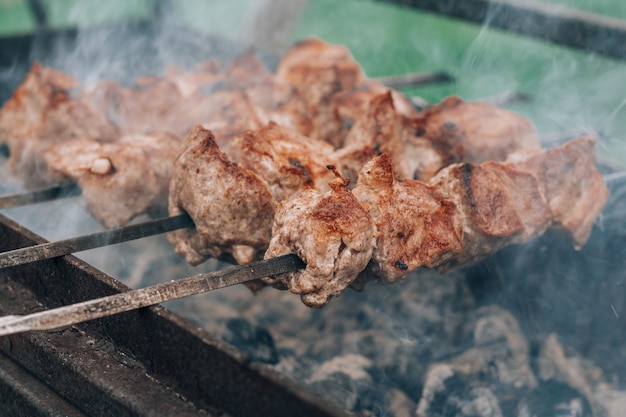 Raw grilled meat on skewers is cooked on charcoal grill, cooking barbecue outdoors