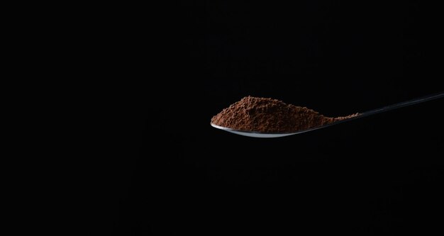 Foto crudo di macinare il cacao o il caffè sul cucchiaino da tè per preparare una tazza o un panificio con sfondo nero