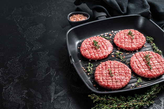 Raw Ground beef meat Burger steak cutlets in grill skillet ready for cooking Black background Top view Copy space