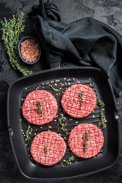 Raw Ground beef meat Burger steak cutlets in grill skillet ready for cooking Black background Top view