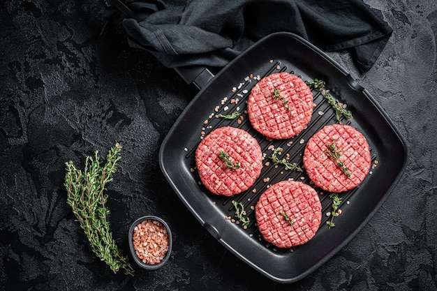 Carne di manzo macinata cruda cotolette di bistecca di hamburger in padella alla griglia pronte per la cottura sfondo nero vista dall'alto