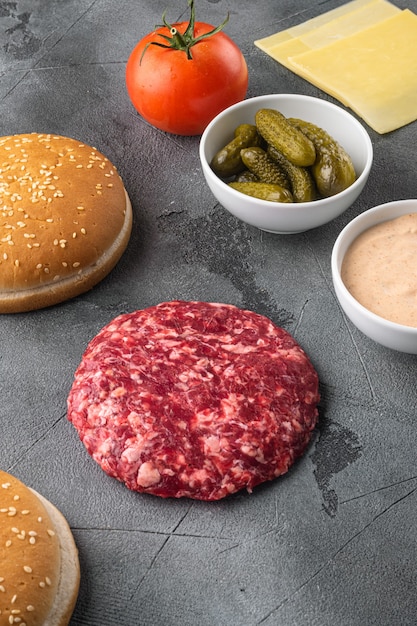 Photo raw ground beef meat burger steak cutlets and seasonings with buns set, on gray stone background