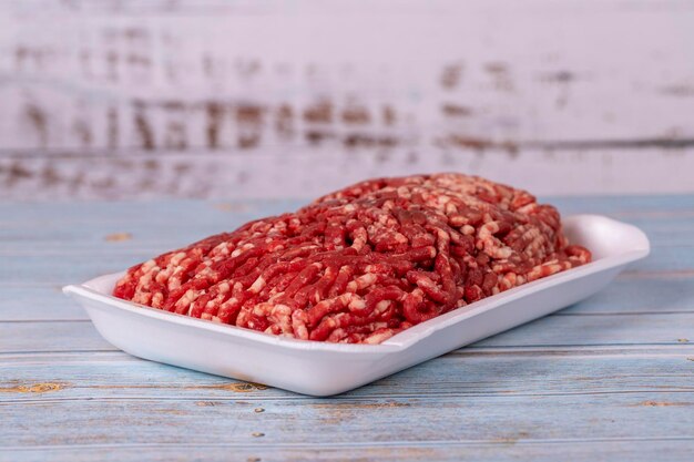 Photo raw ground beef in a white polystyrene tray on a wood background fresh ground beef on wood background