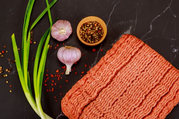 Carne tritata cruda con aglio e la cipolla verde su superficie nera