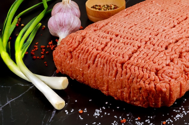 Raw ground beef with garlic and onion on black surface